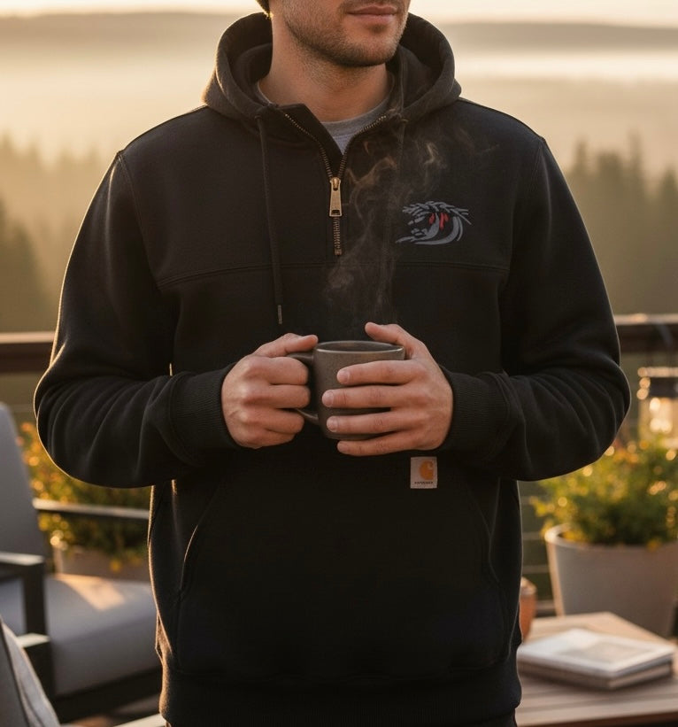 Person wearing a black hoodie with a logo, holding a mug outdoors.