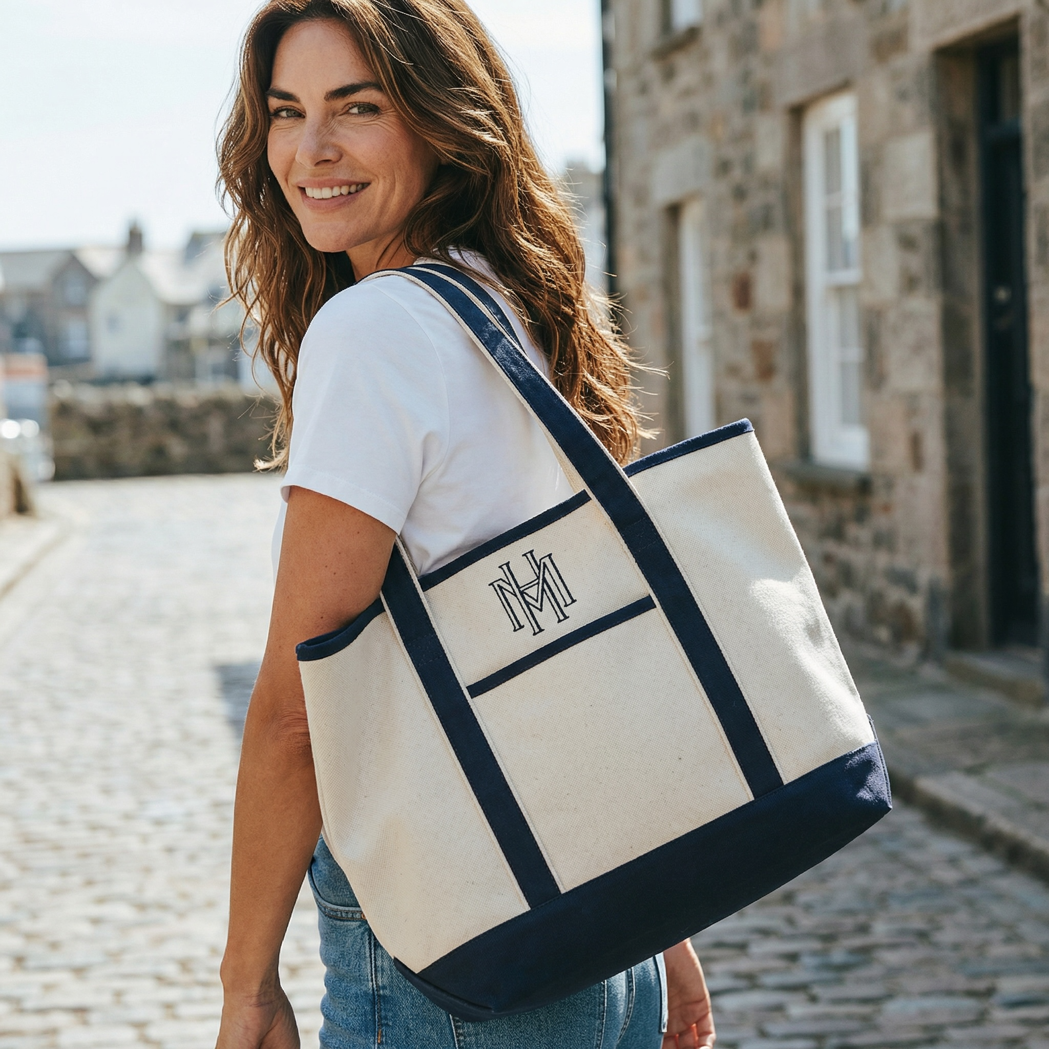 Woman carrying a white tote bag with navy accents and a visible logo, standing on a cobblestone street.