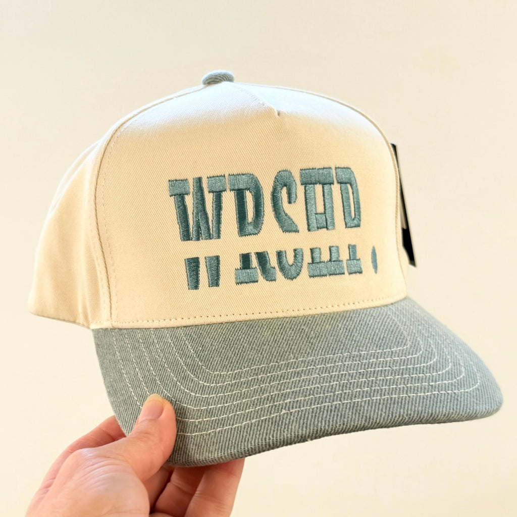Beige and gray cap with text held by a hand against a beige background