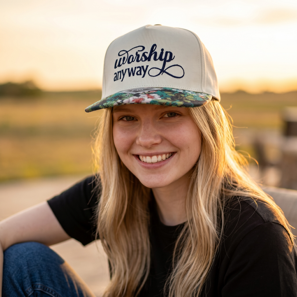 female wearing a cap with 'worship anyway' text in a scenic outdoor setting